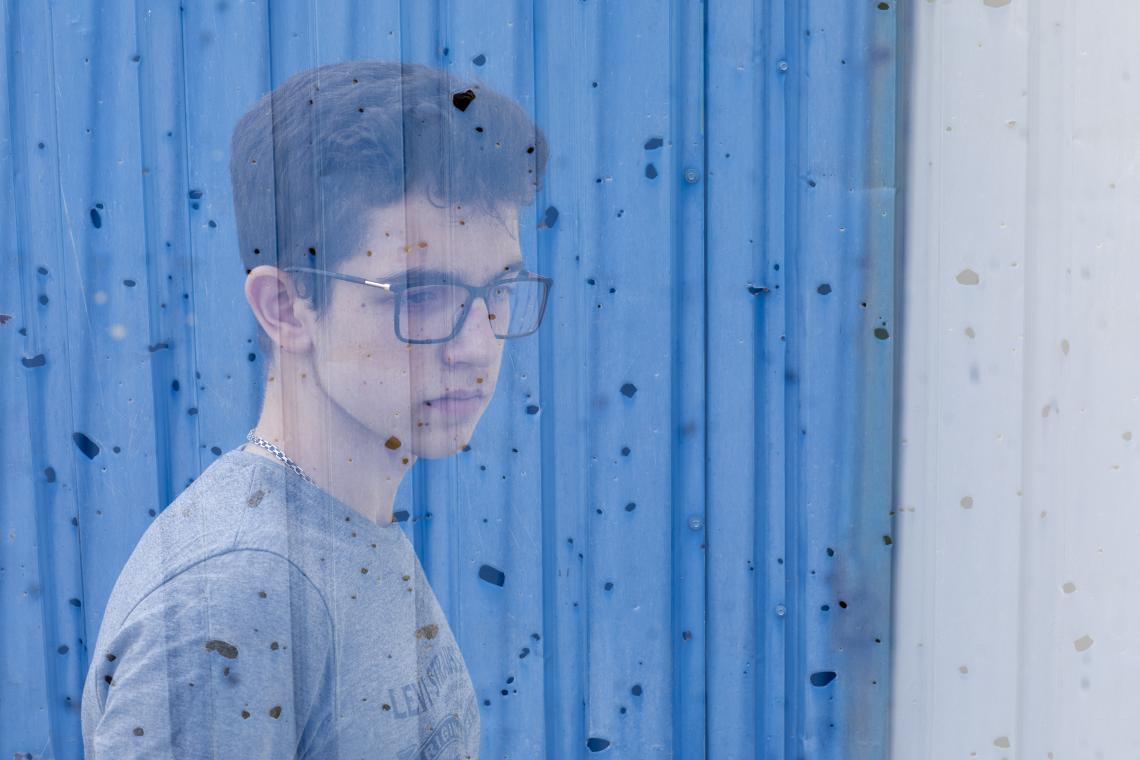 teenaged boy's reflection against a pock-marked wall