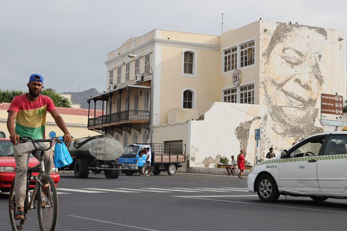 Man riding a bicycle past an image of Cesaria Evora.