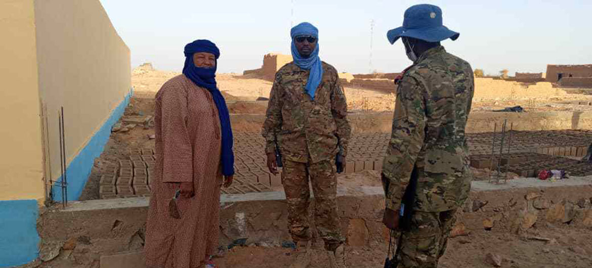 Two men in uniform stand next to a man in civilain clothes