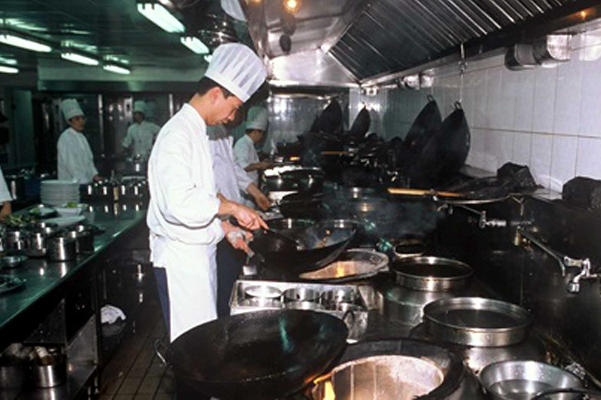 Chefs cooking in a professional kitchen. Some are frying food.