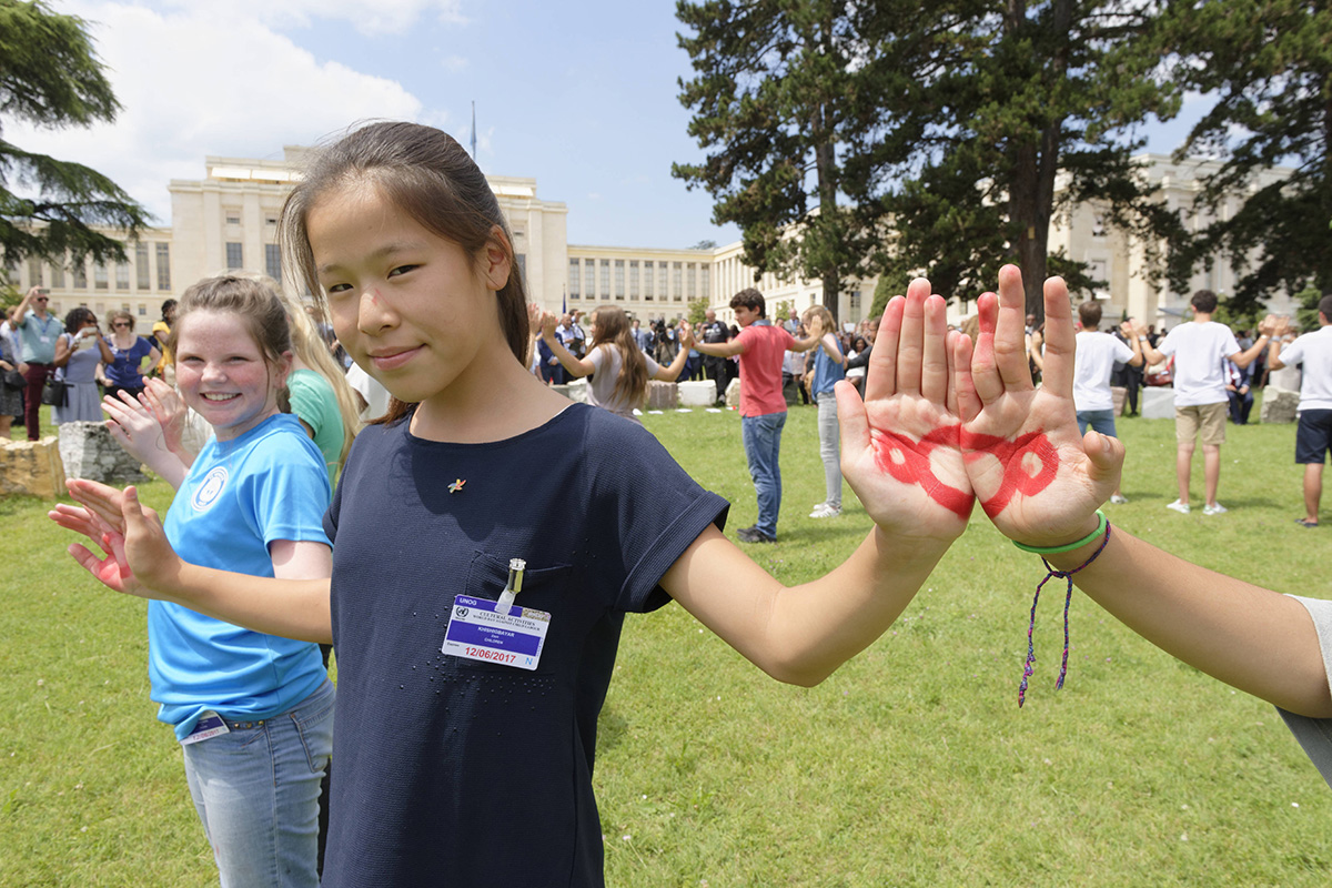 Children put their palms together showing the links painted on them as they form a circle. 