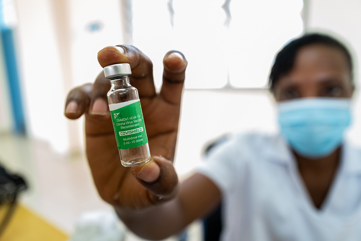 A health worker wearing a facemask holds out a used vile of COVID-19 vaccine.