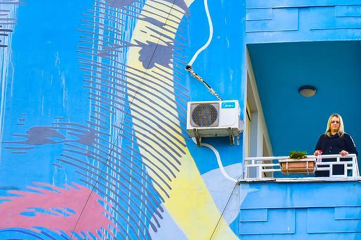 A woman from her balcony next to a mural on the wall.