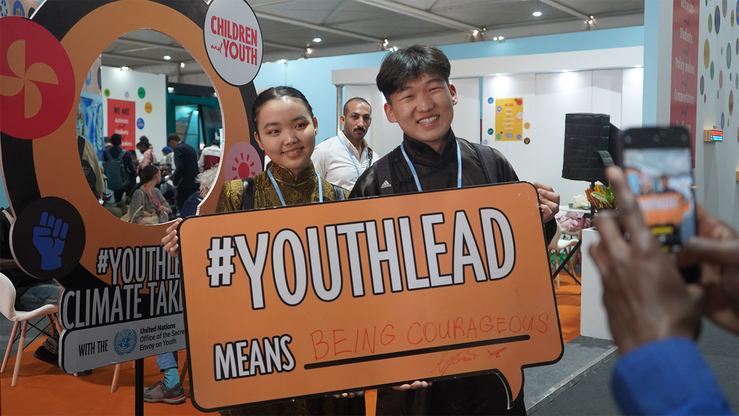 Two young people holding a sign written youthlead, smiling to the camera