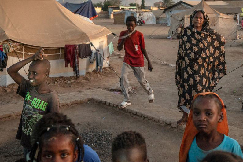 A group of children and a women between tents of a camp for displaced people