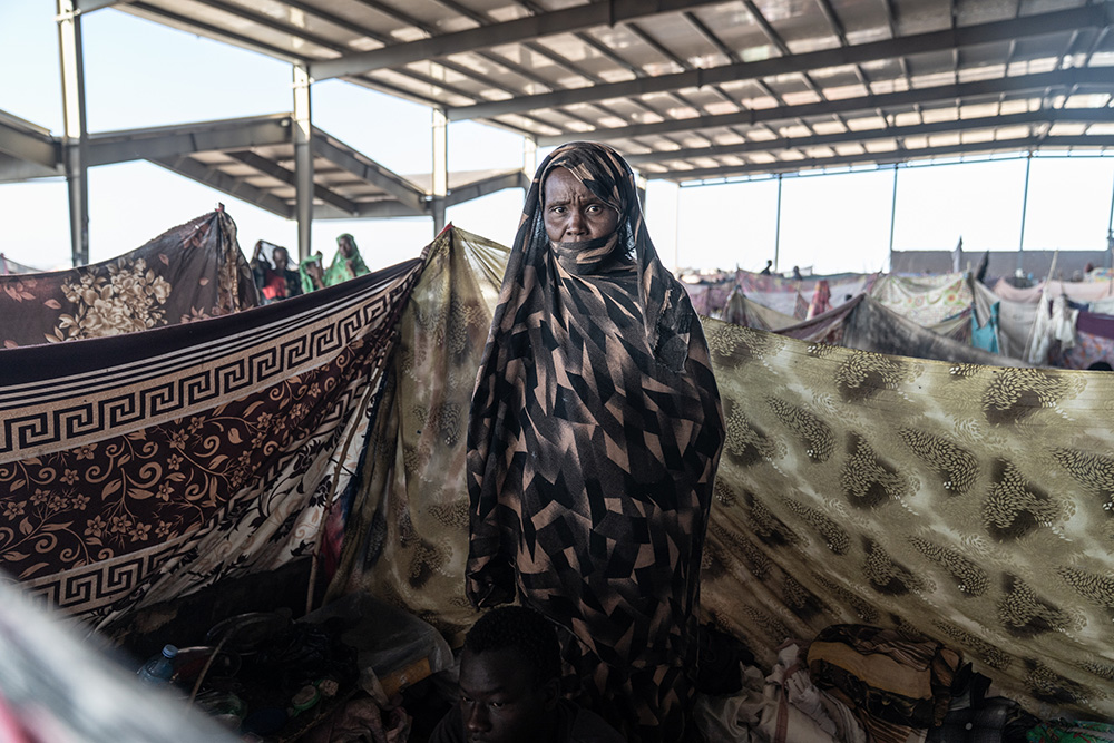 a worried woman standing in her makeshift corner of a crowded shelter