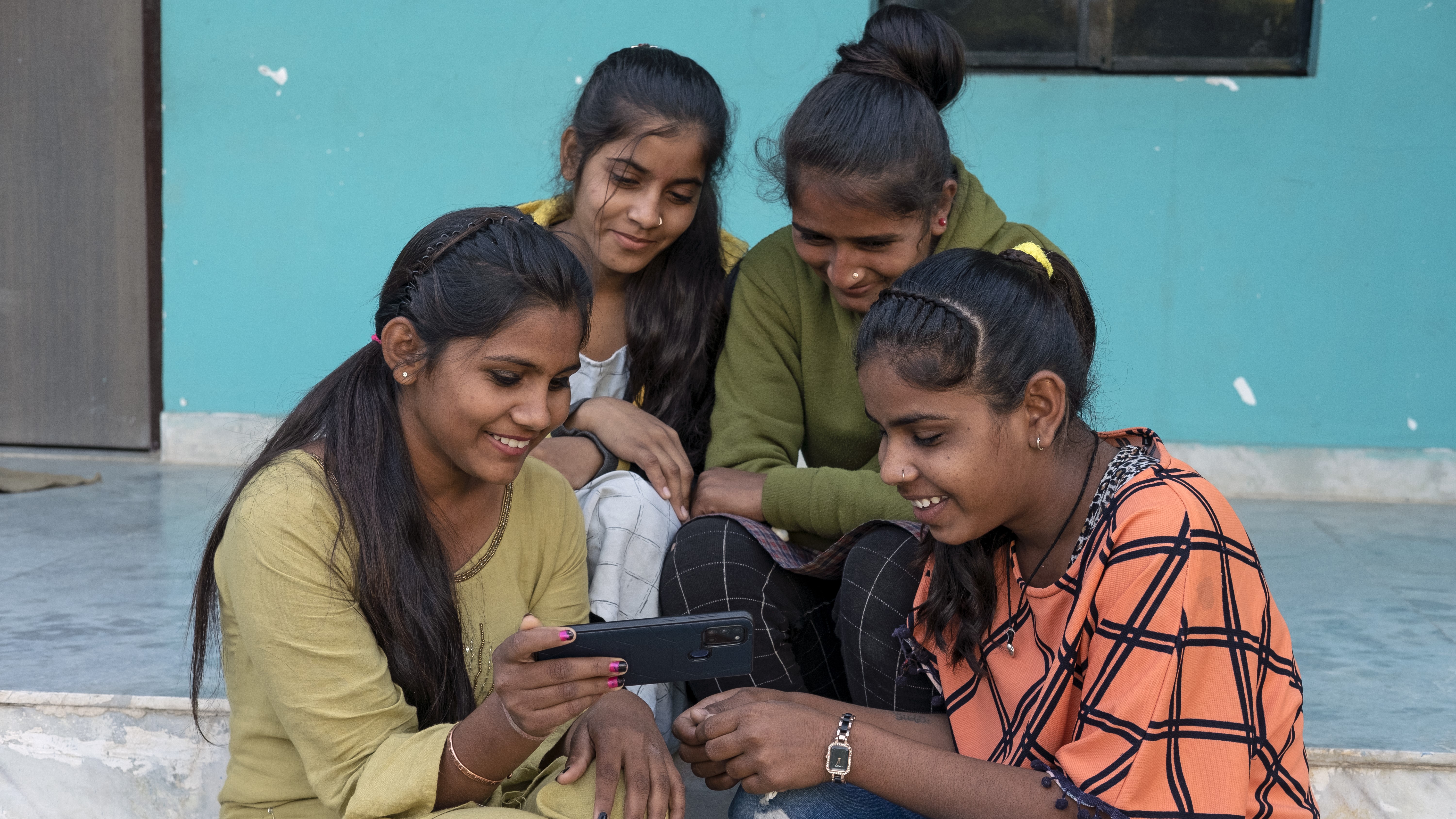 Un groupe d'adolescentes assises sur des marches regarde l'écran d'un téléphone portable.