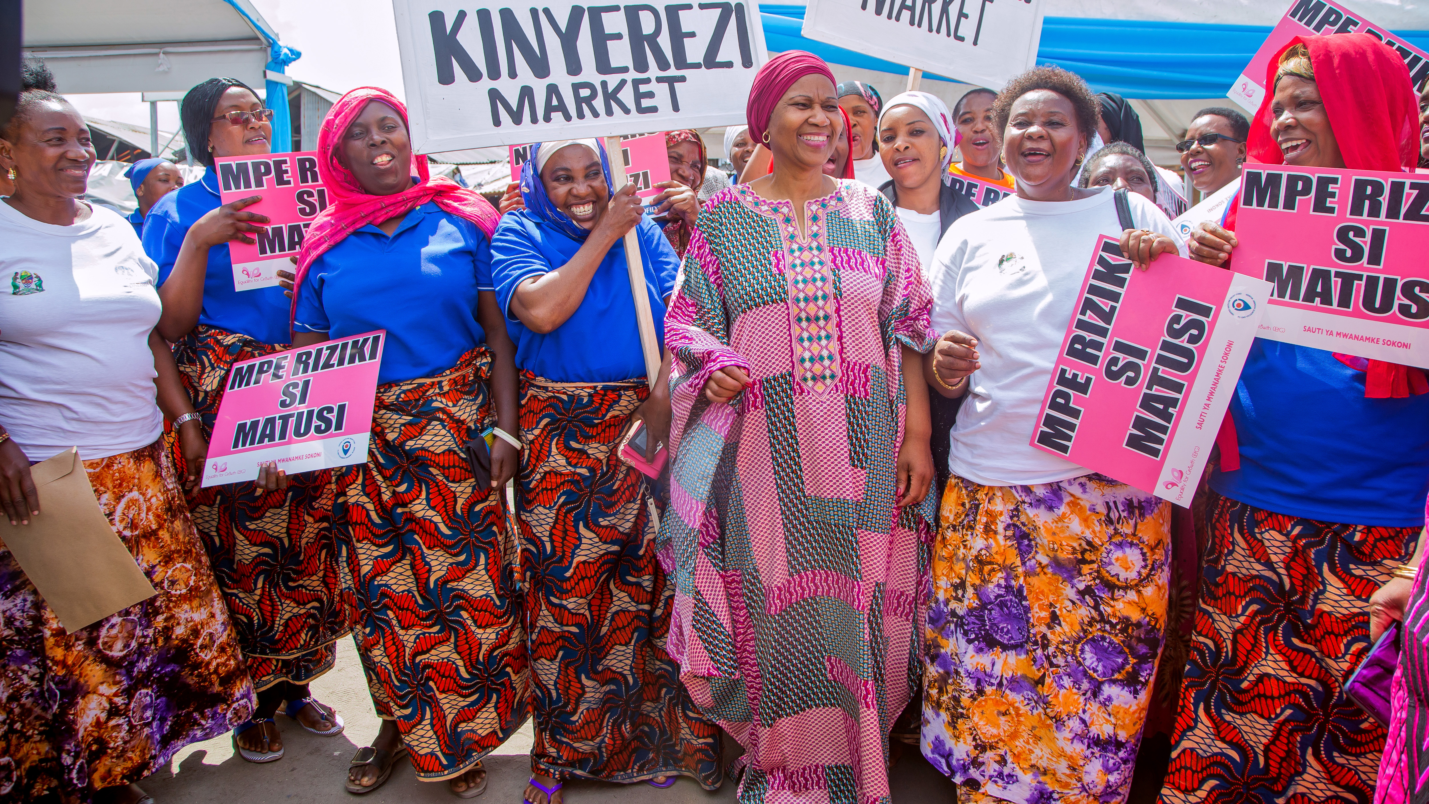 Phumzile dressed in bright traditional African clothes is surrounded by African women holding up signs.