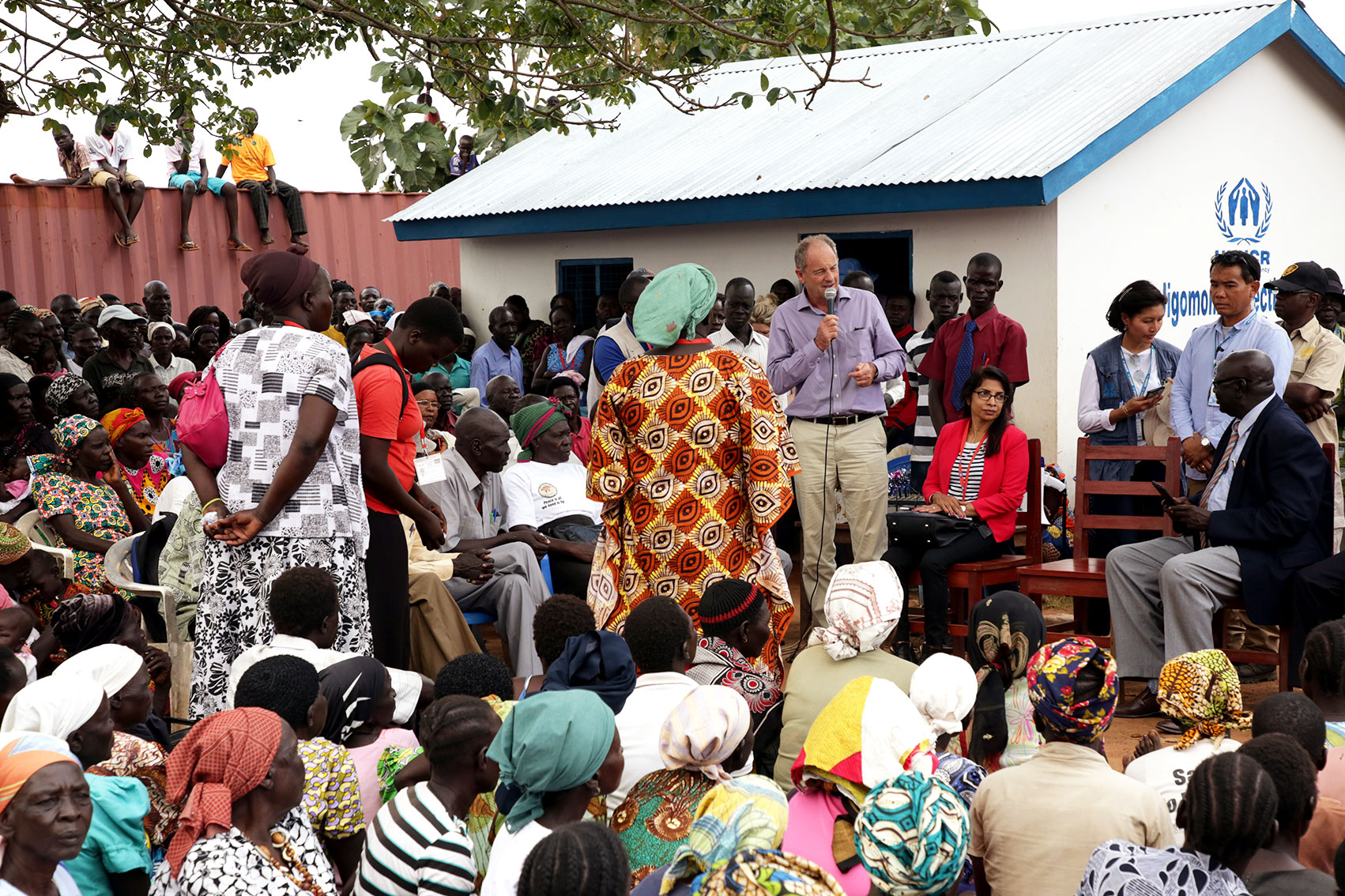 David Shearer speaks to a very large group of people in the outdoors. A UNHCR marked building is in the background.