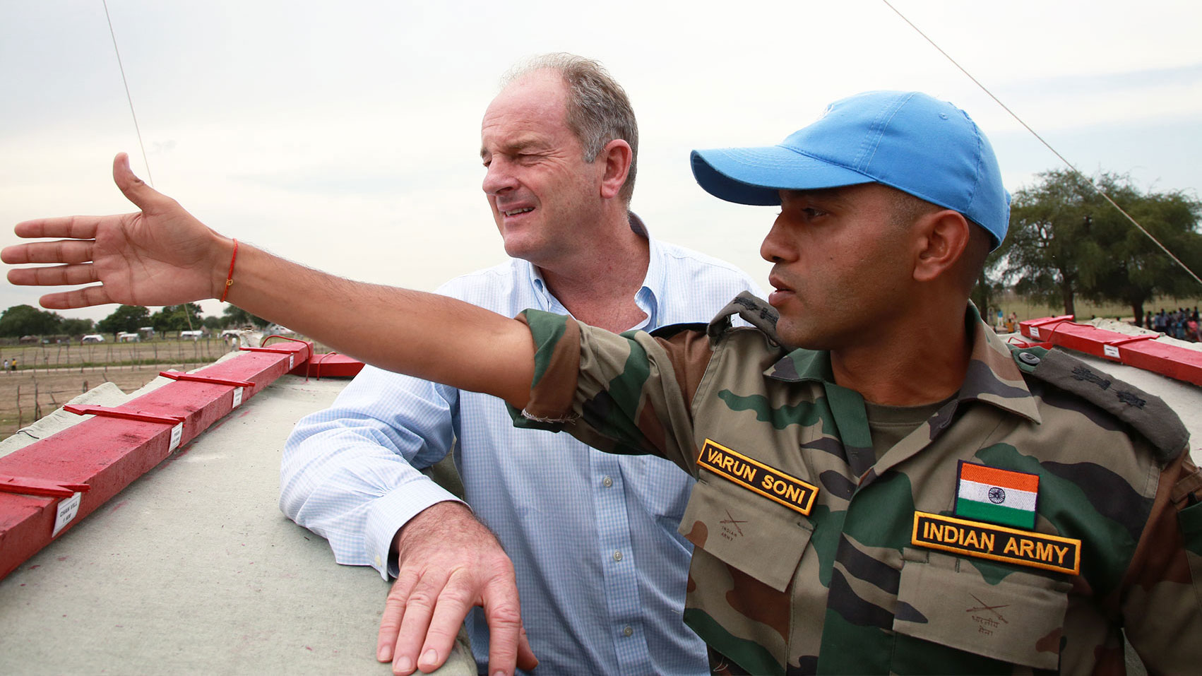 An officer from the Indian army is on a rooftop with David Shearer. The officer is pointing left and both men are looking in that direction.