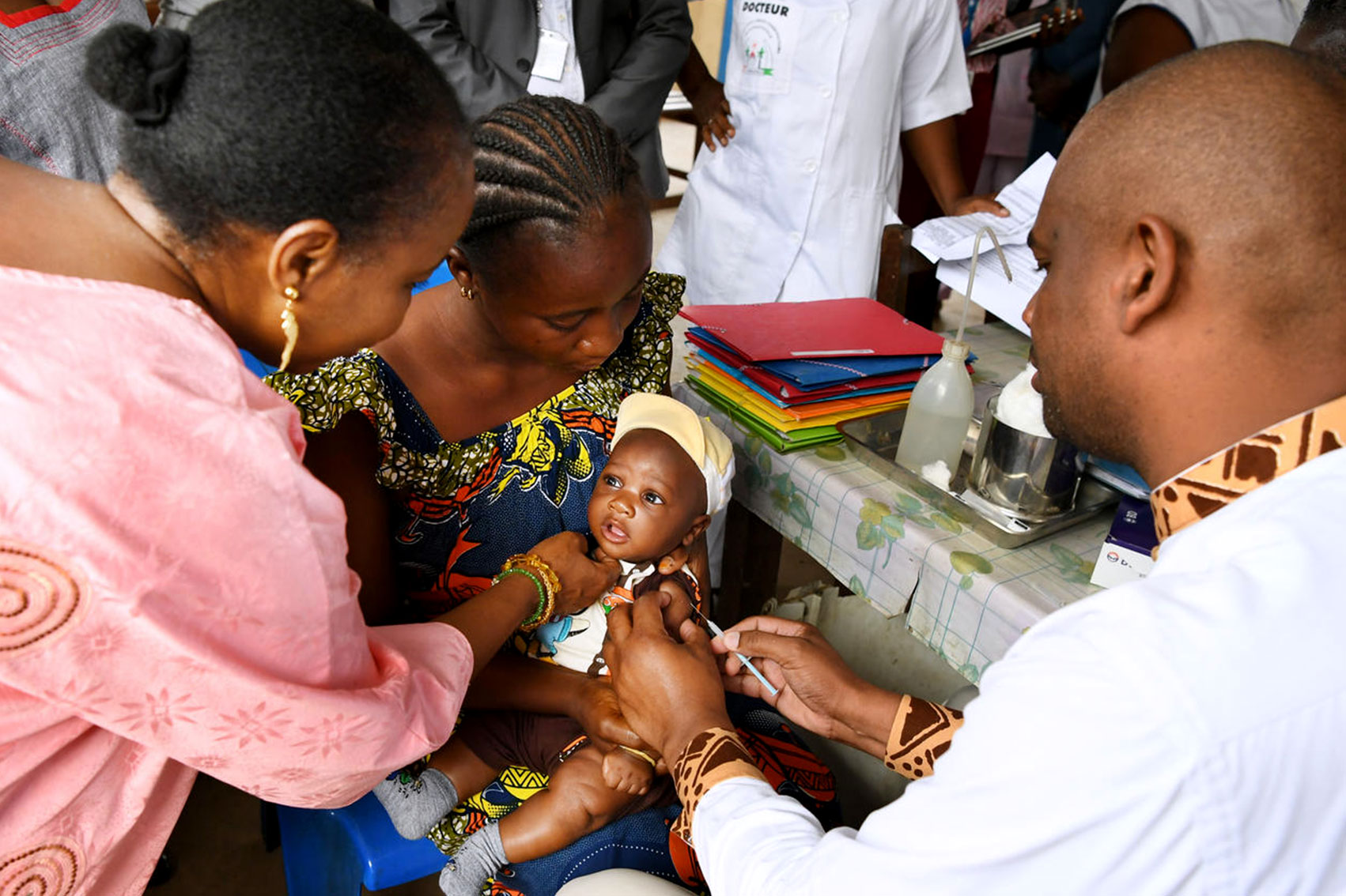 A woman distracts a baby while Aboubacar administers a shot to the child's arm.