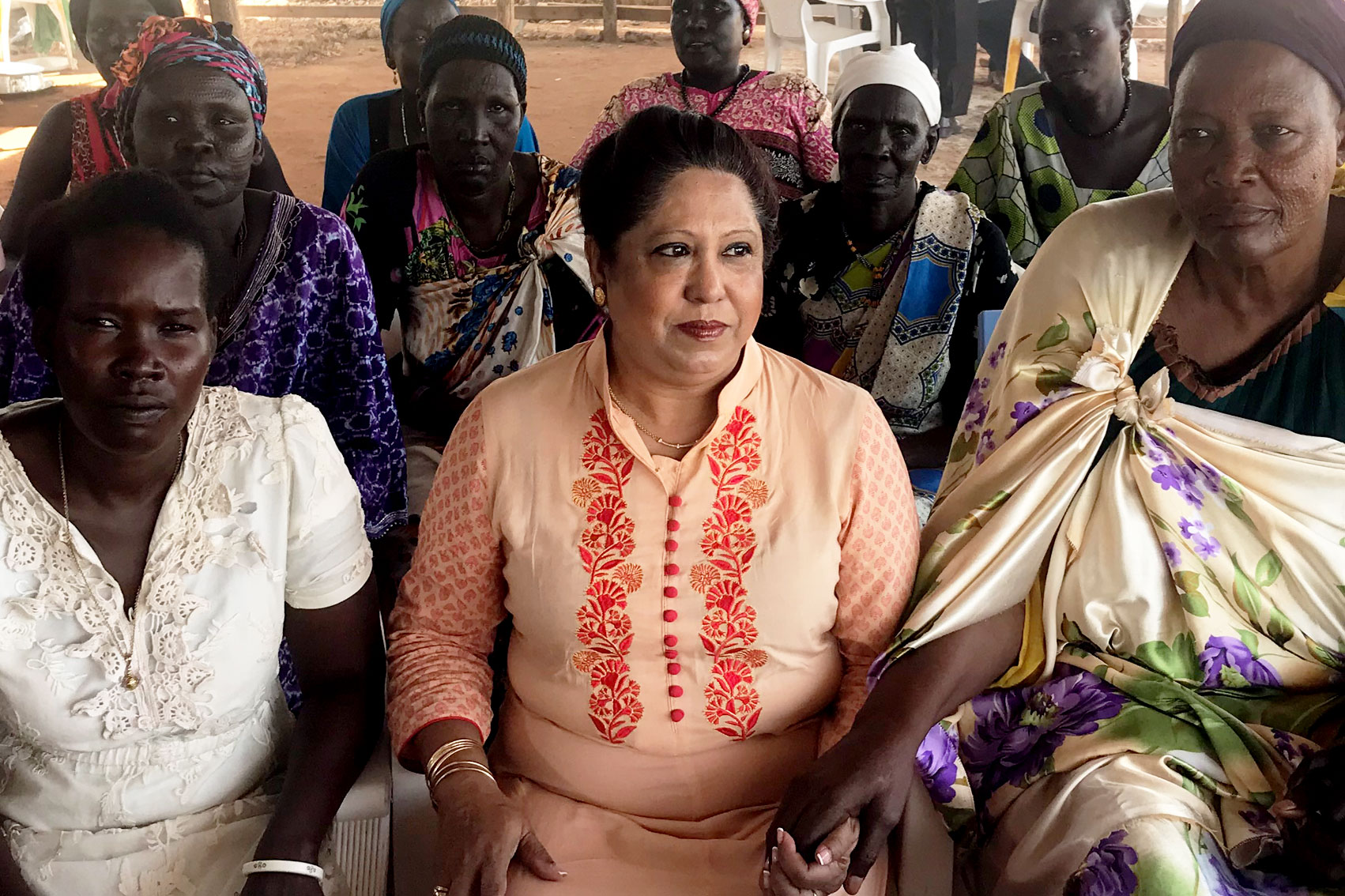 Pramila Patten sitting with many women holding their hands as they tell their harrowing srtories.