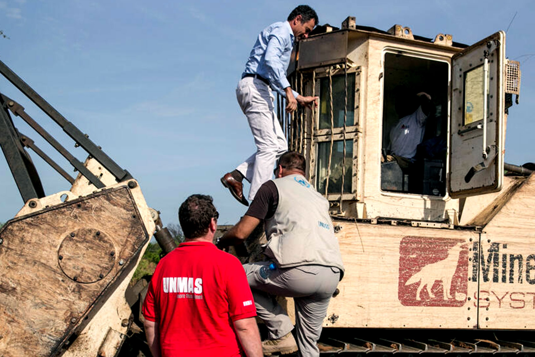 Three men climb a mine-clearance machine to inspect it.