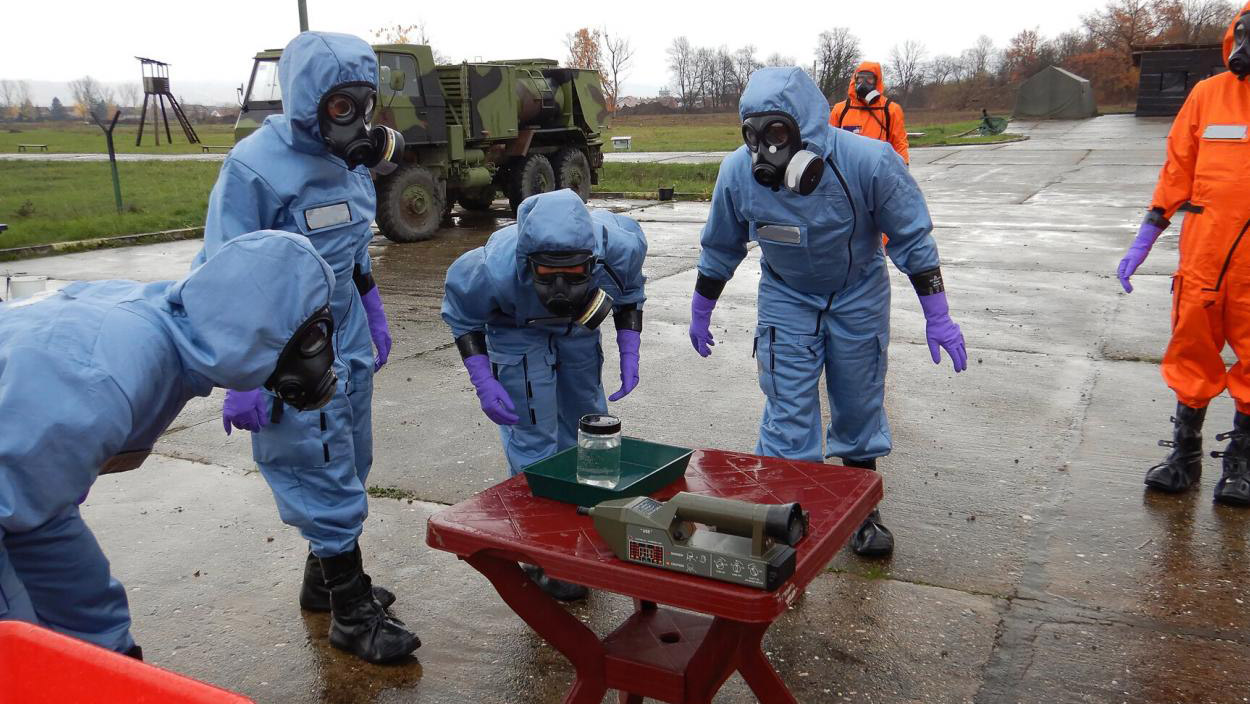 people in protective gear inspecting liquid