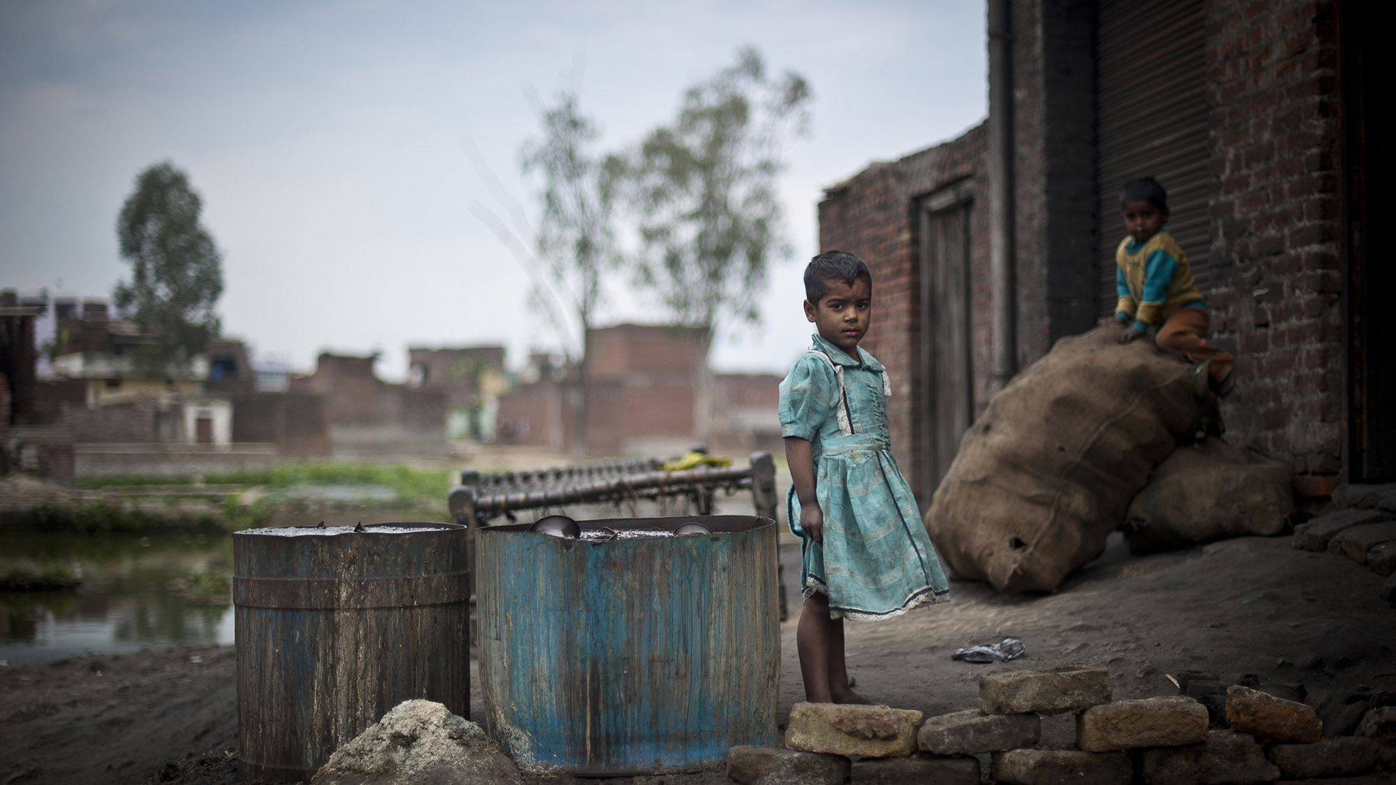 Des enfants jouent devant un atelier de polissage de métaux en Inde.