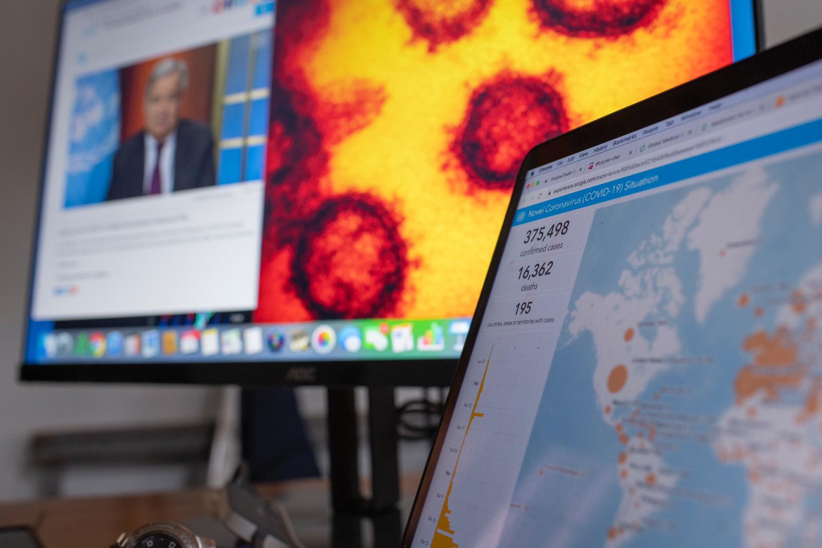 Two computer monitors are in view: one with a map and corresponding local COVID data; the other has an image of the UN Secretary-General delivering a speech whilst next to him is a screen shot of the COVID virus.