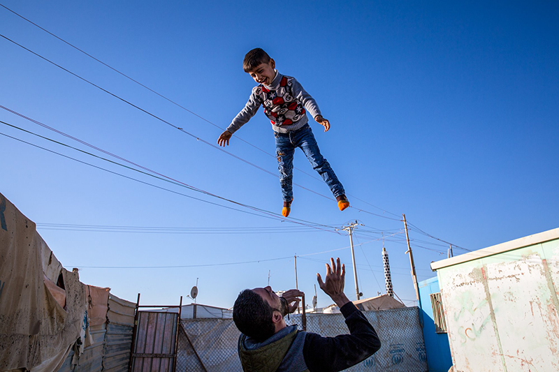 a father at a refugee camp throws his son in the air