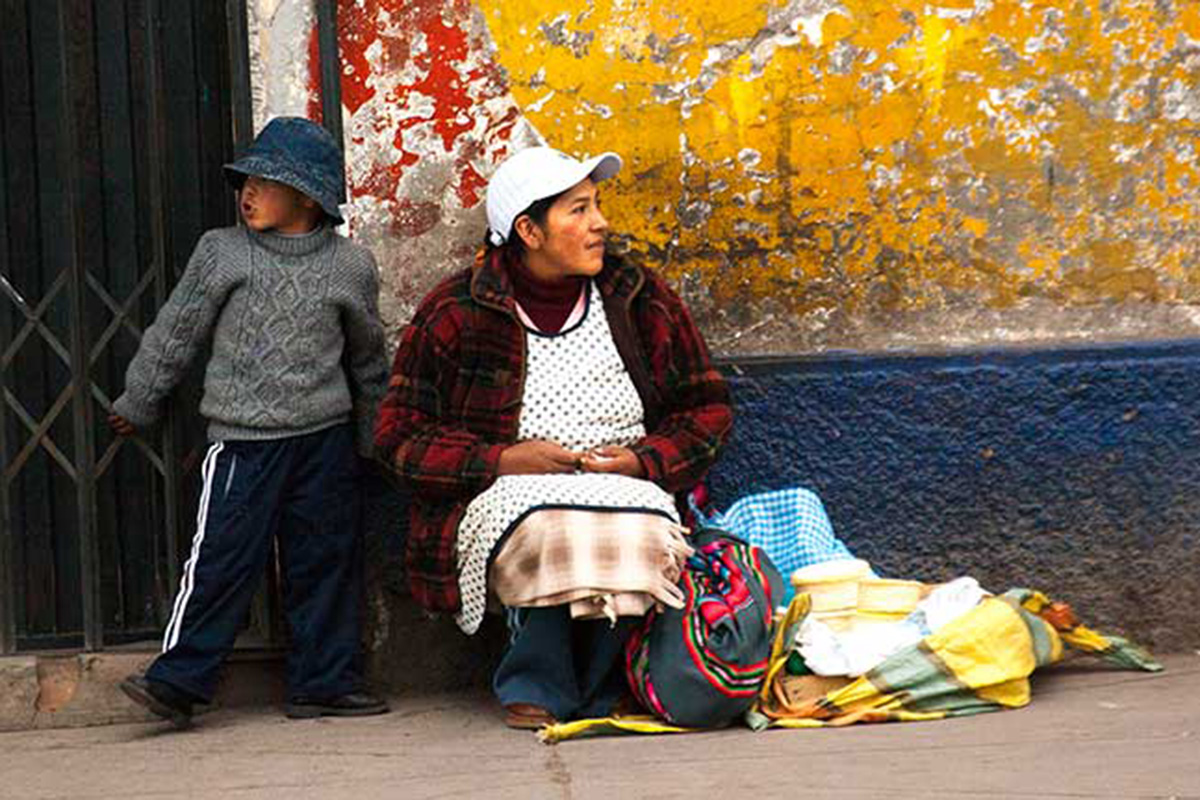 A woman sits on the sidewalk with a boy besides her.