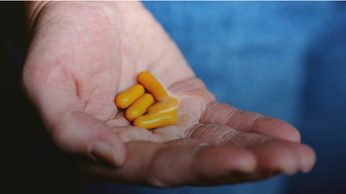 A hand holds a yellow pill