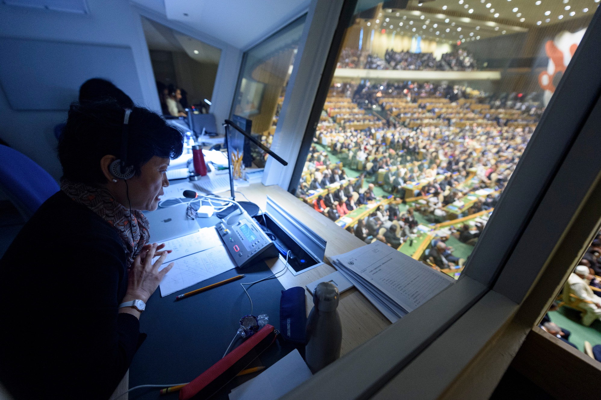 A woman sits inside a booth facing the floor of the General Assembly.