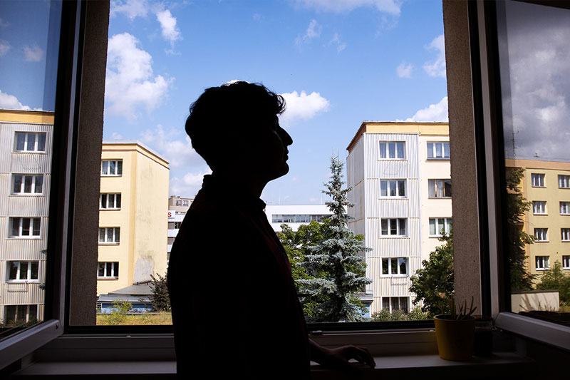 photo of a dark silhouet of a person with short hair set against a window overlooking blocks of apartment buildings