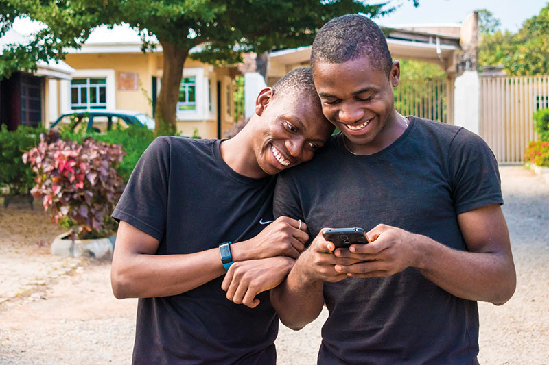 Two men embrace sideways while looking at a cell phone