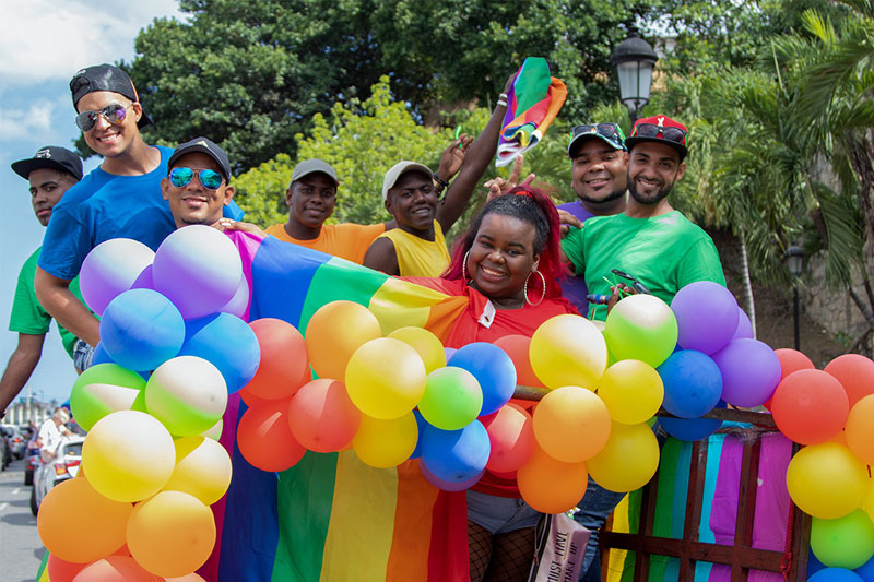 photo of people standing together in the outdoors holding colorful rainbow balloons and a rainbow flag
