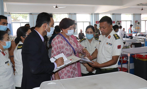 man and woman taking notes as they are surrounded by people and talk to an officer in uniform inside a hospital