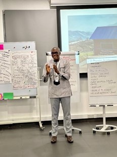a man giving a talk with posters and a projection behind him