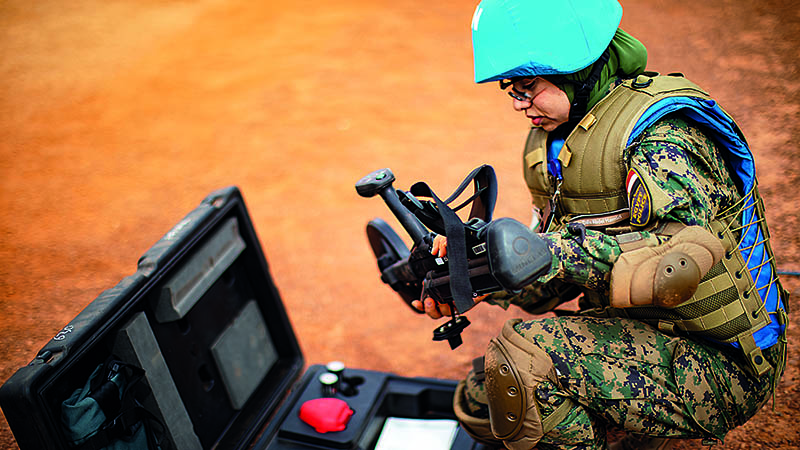 pdf annual report A woman peacekeeper in camouflage clothes and a blue helmet kneels in front of a black suitcase and looks at the black scanning device in her hands.