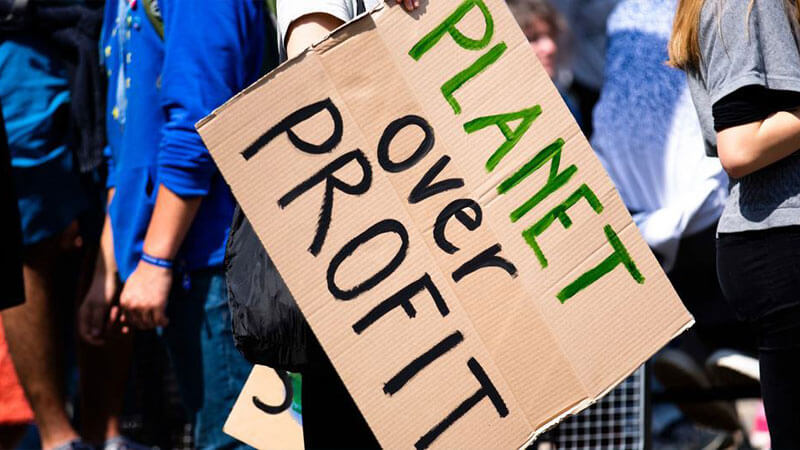 A closeup of a protest, with someone holding a sign where written planet over profit