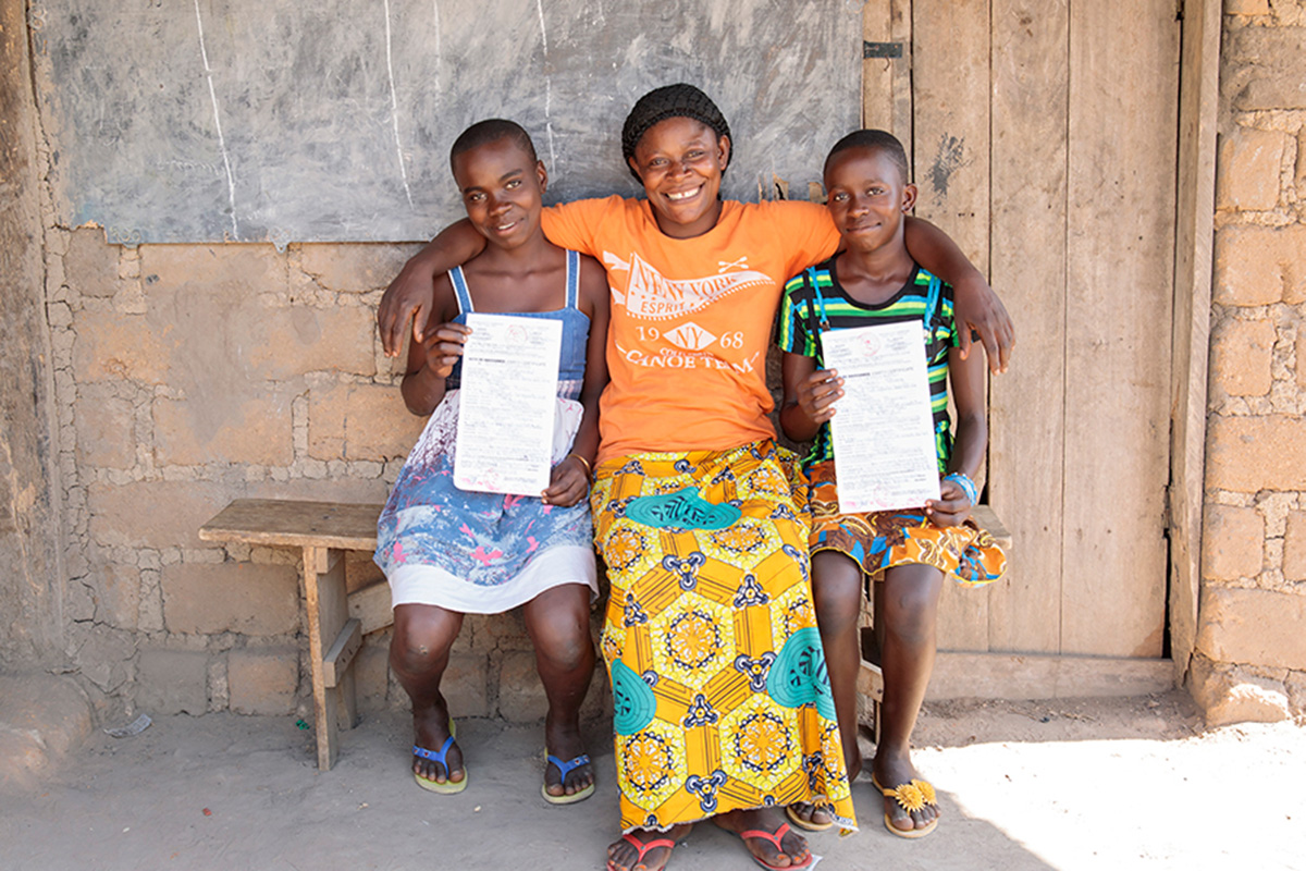 two girls sit on each side of their mother as they hold up their birth certificates