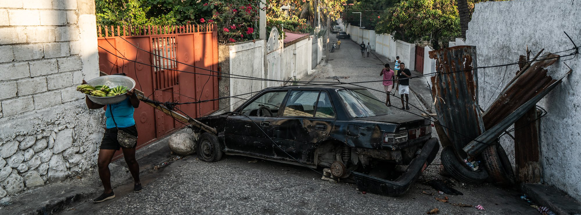 view of a street where a few pedestrian walk around a burnt car and some tires