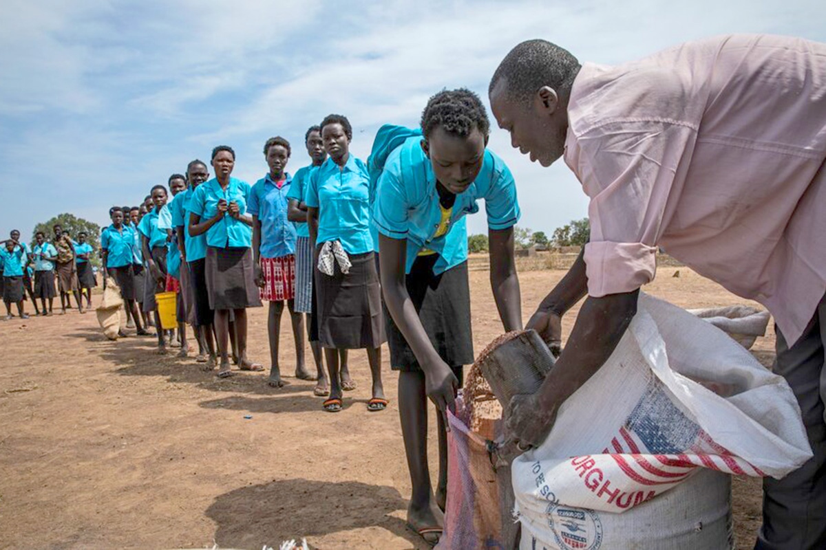 A line of girls in uniform wait for food rations. 