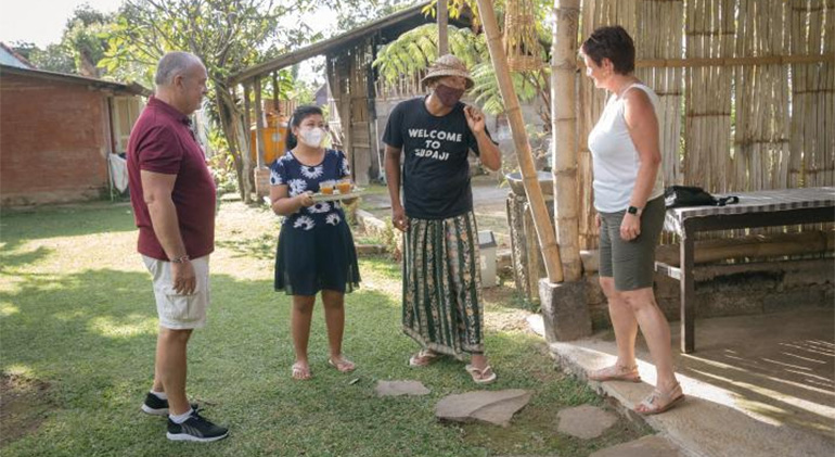 Dekha Dewandana et sa femme Luh Sarry Shantika Dewi se tiennent dans le jardin de leur maison d'accueil et discutent avec deux touristes étrangers.