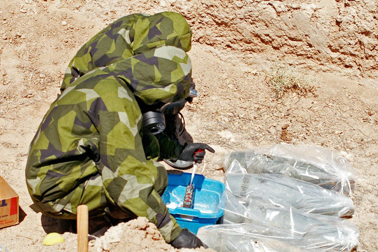 UNSCOM inspectors take mustard agent samples from 155-mm mustard agent artillery projectiles, which have been wrapped in plastic to minimize contamination, Iraq, 1991.
