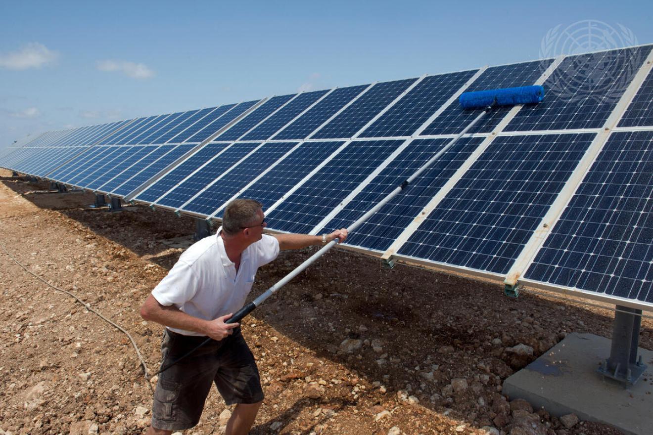 A solar farmer cleans a row of solar panels