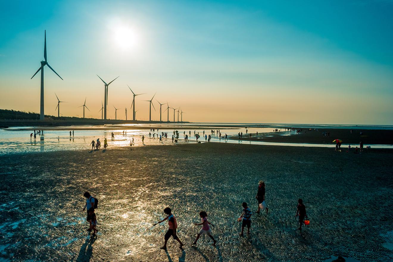 people cross through a field with wind turbines