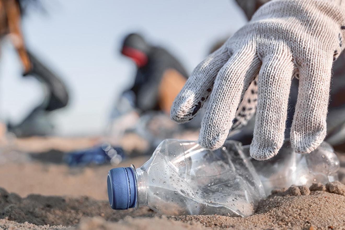 Primer plano de una mano con guantes recogiendo una botella de plástico en una playa
