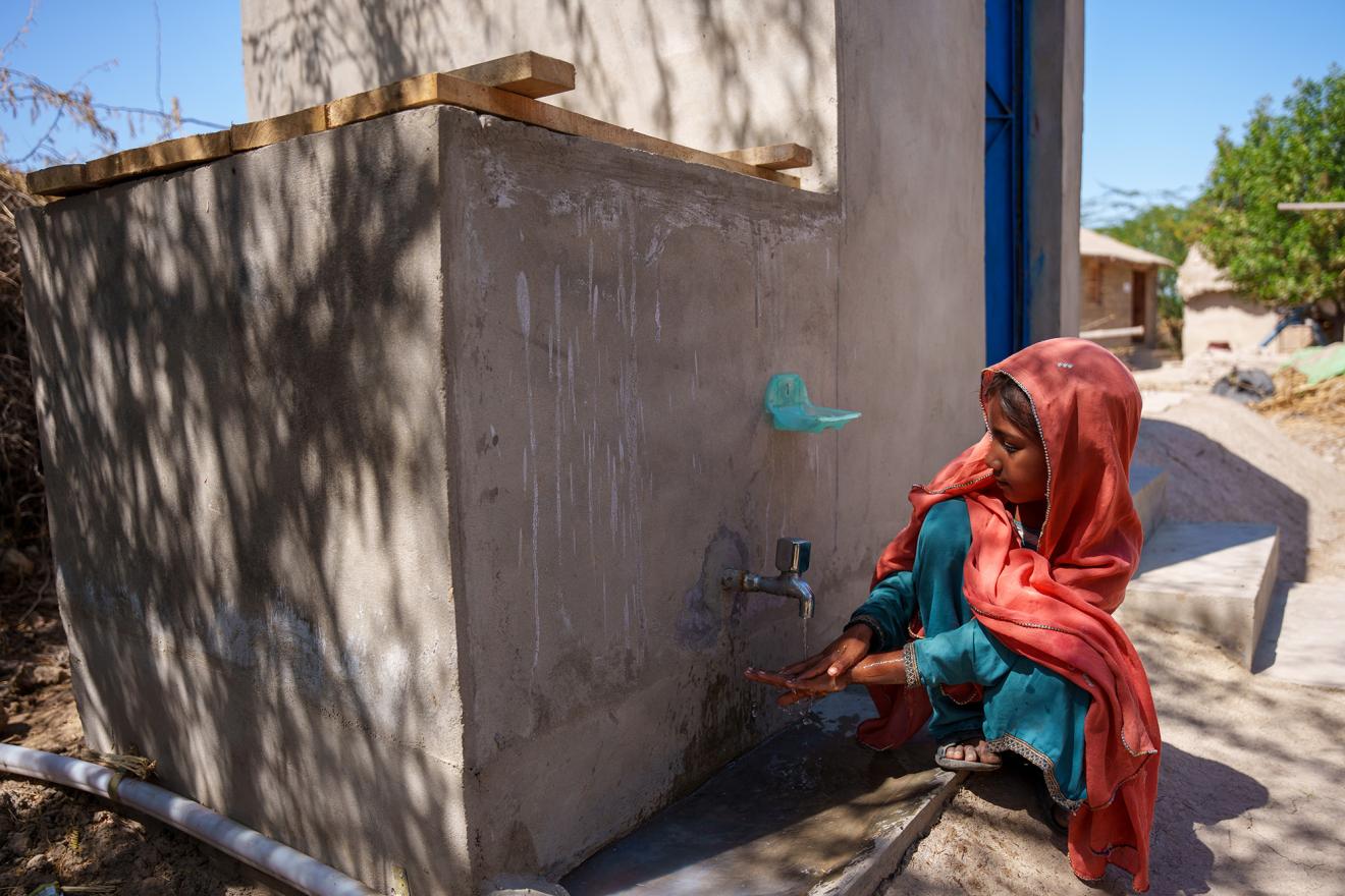 A Pakistani girl washes her hands in front of a latrine. 