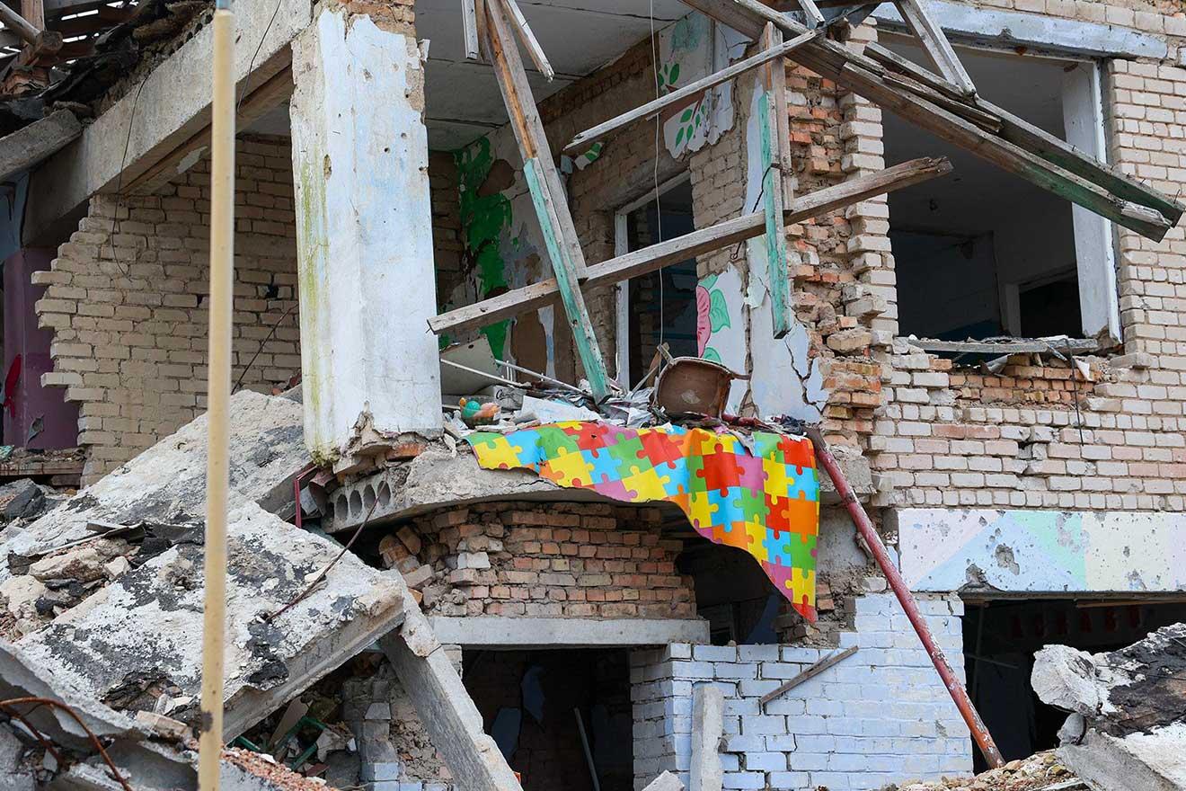Un tapis coloré pour enfants et d'autres jouets sont visibles au milieu des ruines de la façade d'un bâtiment à moitié détruit