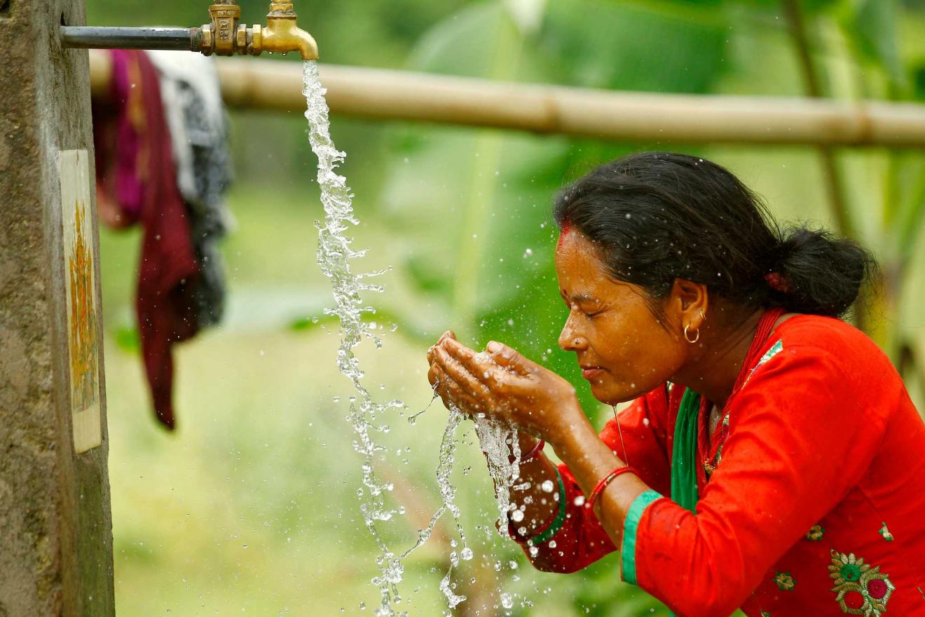 Une femme se lave le visage sous un robinet d'eau courante