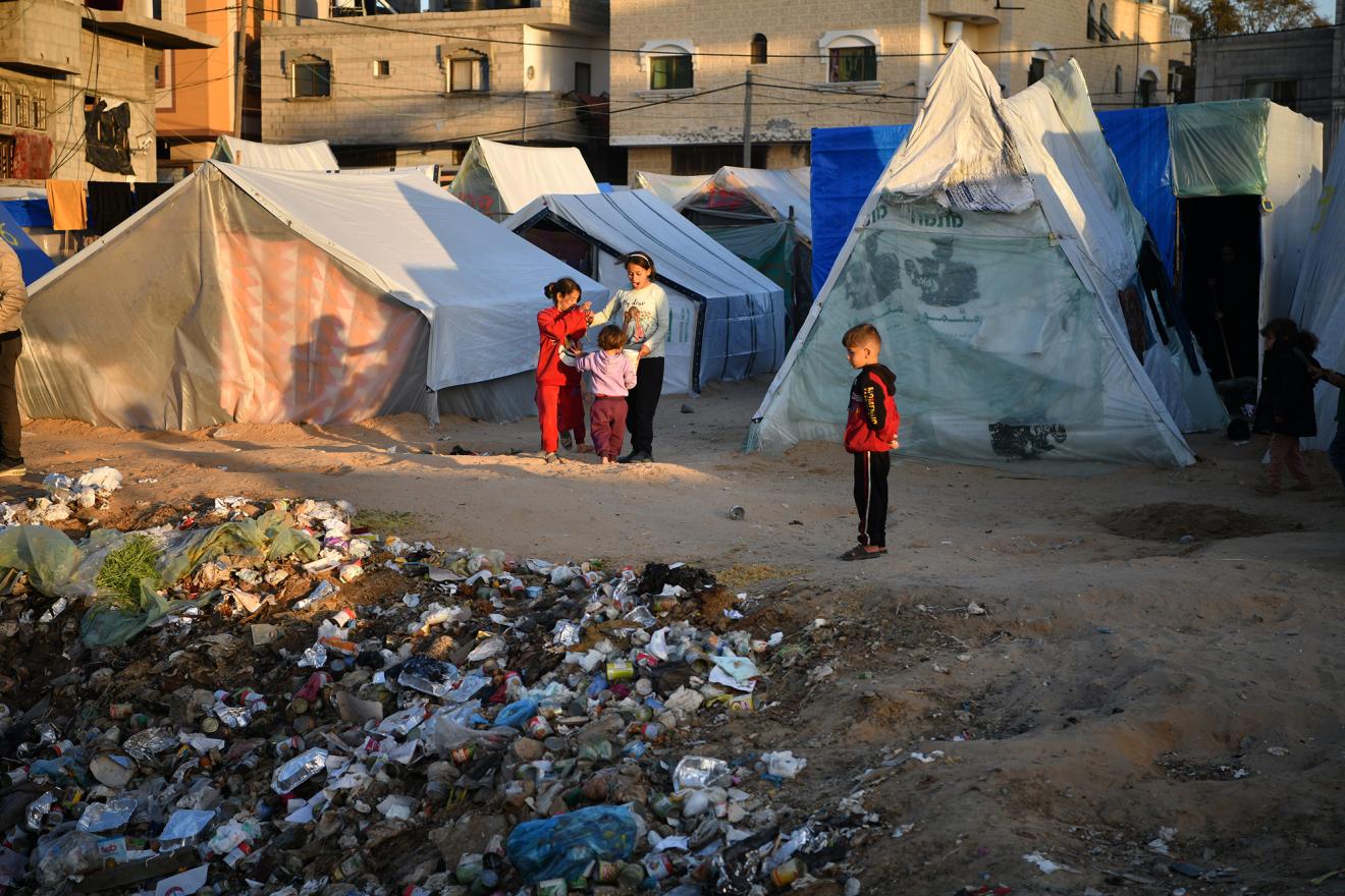 A group of young Palestinian kids living in tents next to a large amount of solid waste.