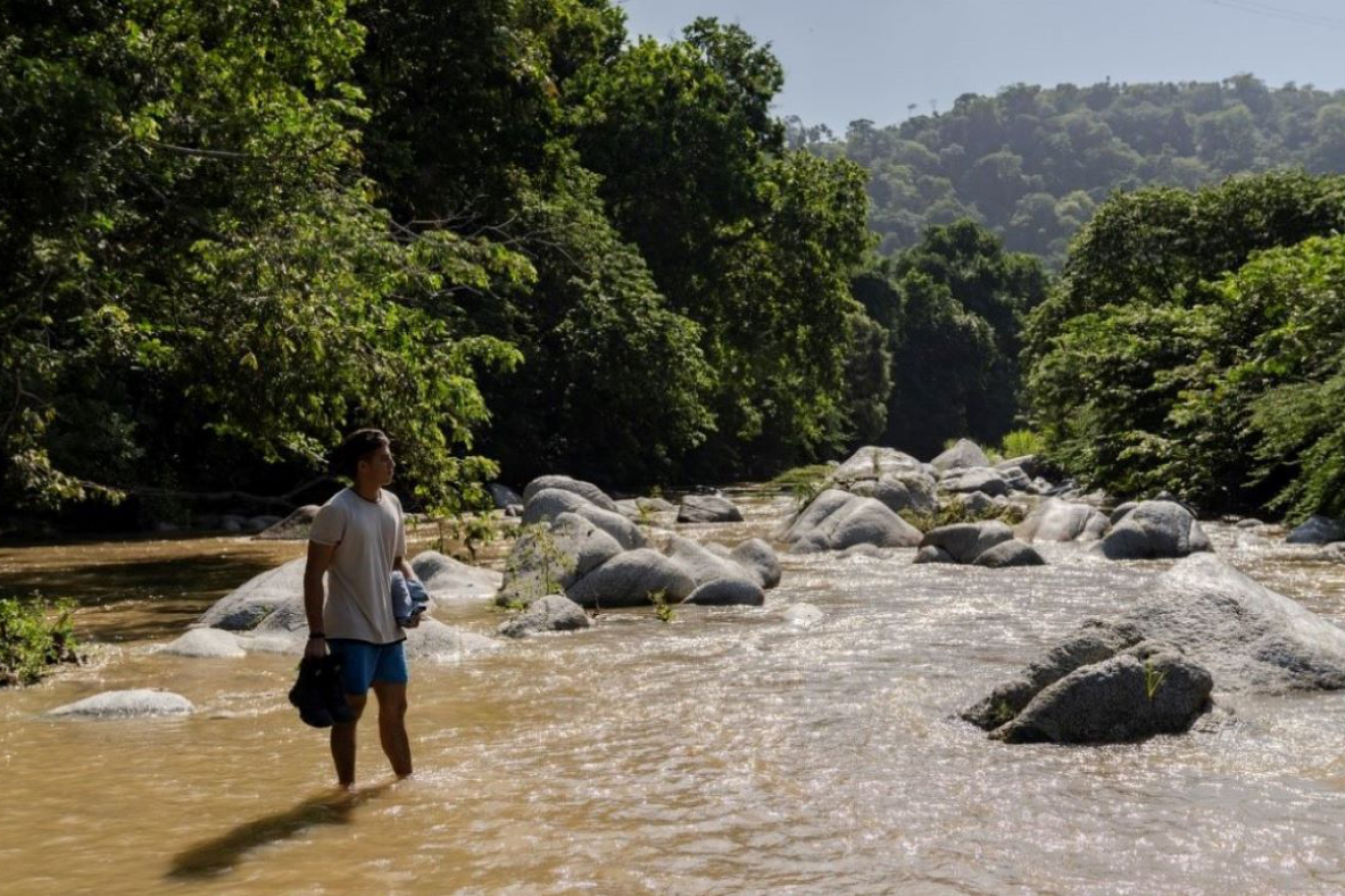 Un homme se tient au milieu d'une rivière dans une vallée, l'eau lui arrive aux chevilles