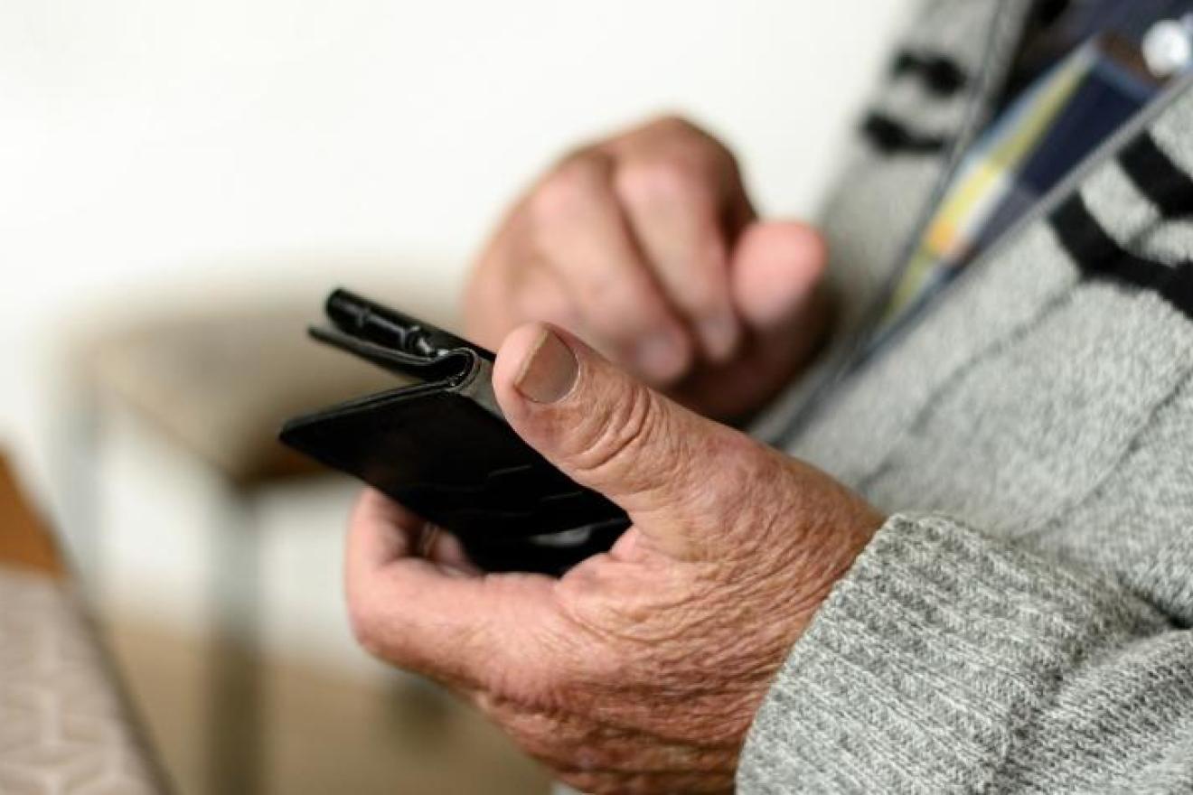 Las manos de una personas mayor manejan un teléfono móvil.