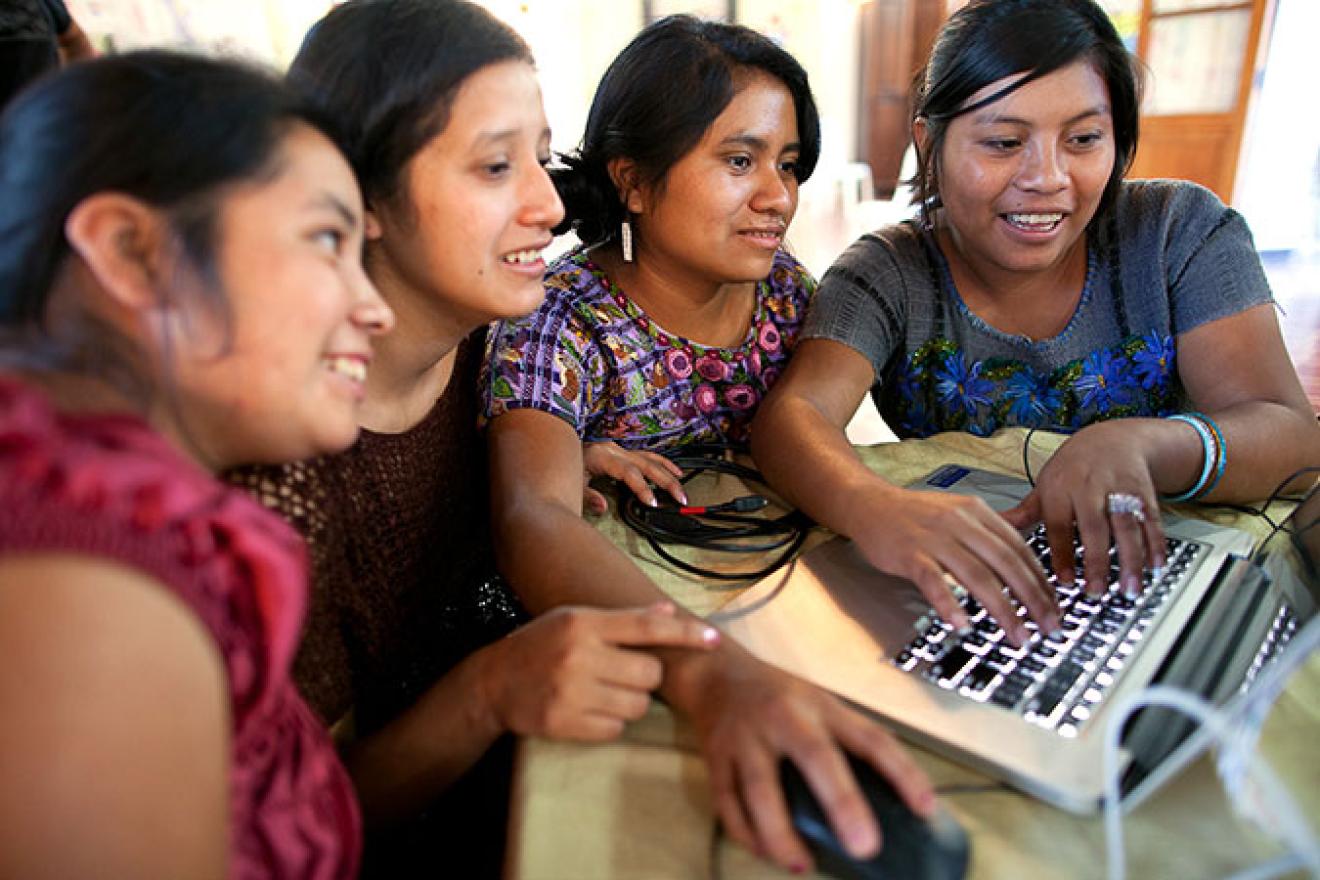 Un grupo de cuatro mujeres jóvenes trabaja en torno a un ordenador portátil. 