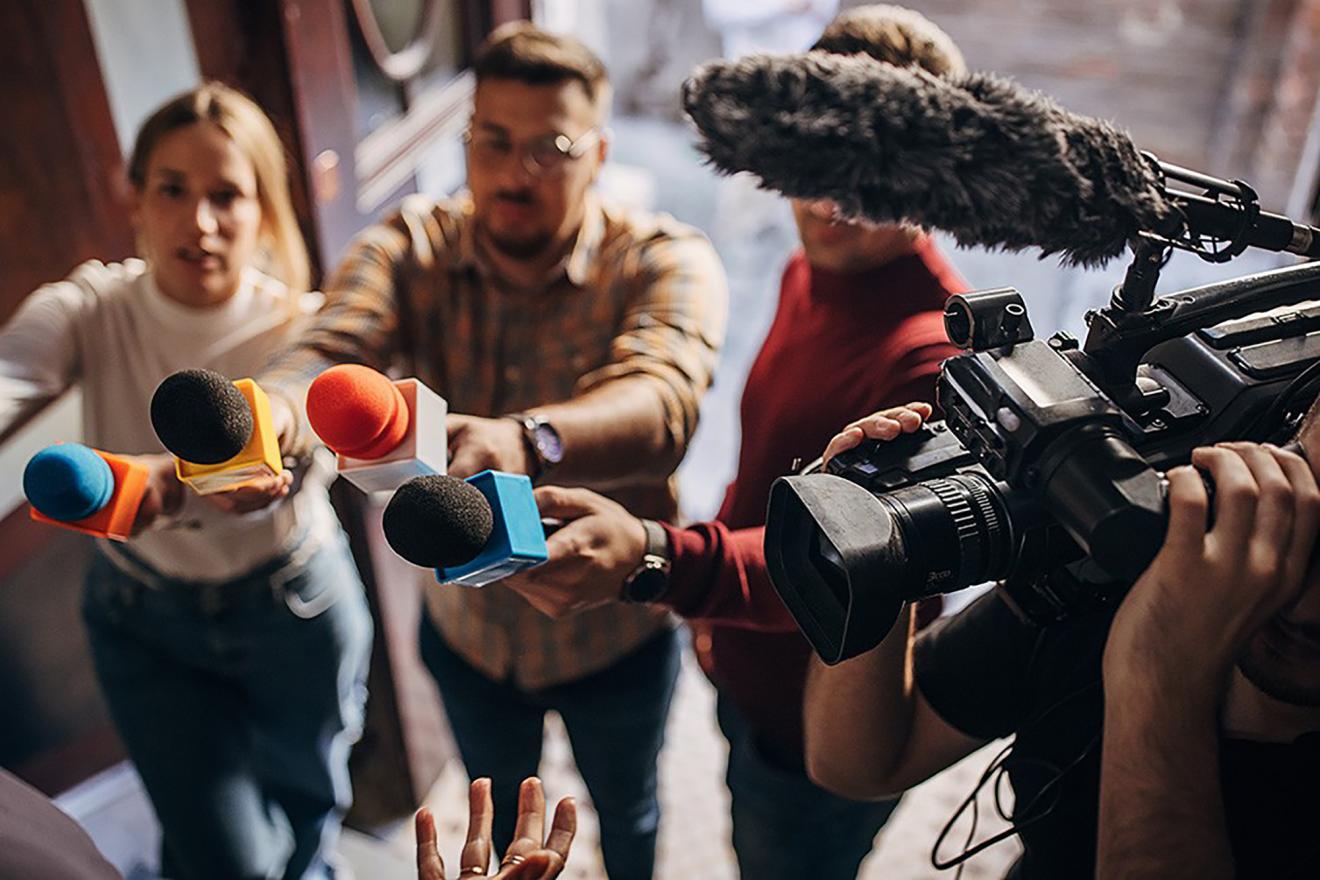 Un grupo de periodistas extiende sus micrófonos hacia una persona que no se puede ve en la imagen.