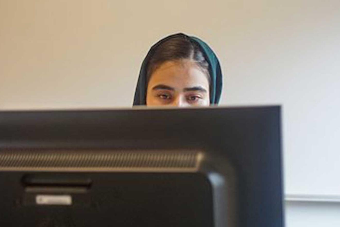 Le visage d'une jeune fille portant un voile s'aperçoit derrière un écran d'ordinateur