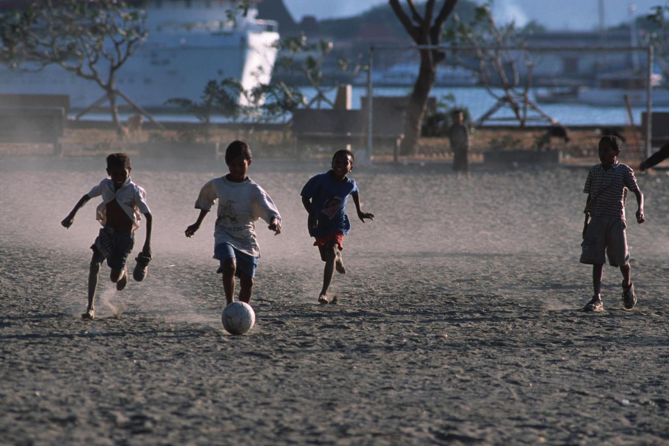 De jeunes enfants jouent au football sur un terrain poussiéreux