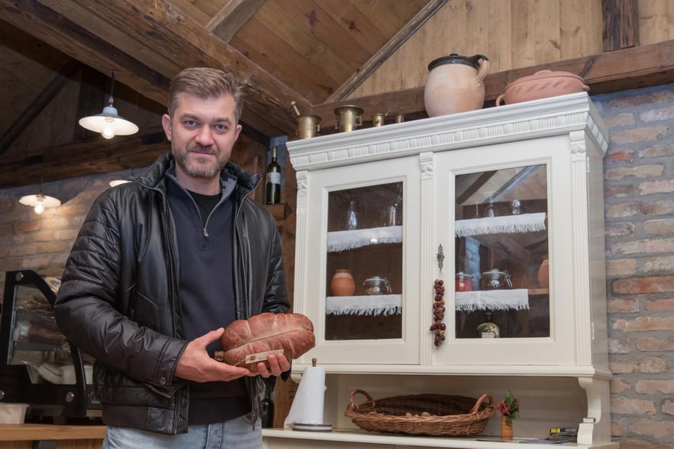 A man with a traditional Croatian sausage in his hand in a kitchen.